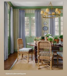 a dining room with green walls and wicker chairs around a table in front of two windows