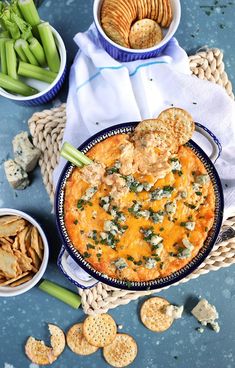 a bowl of cheese dip with crackers and celery on the side next to it