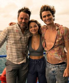 two men and a woman posing for a photo on a boat with the ocean in the background