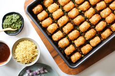 a pan filled with tater tots next to bowls of sauce and condiments