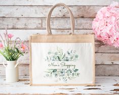 a shopping bag sitting on top of a wooden table next to flowers and a vase