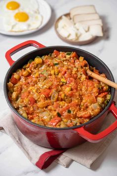 a red pot filled with food on top of a white counter next to an egg