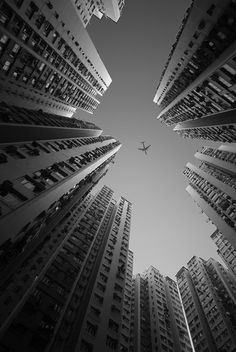 an airplane is flying through the air between tall buildings in black and white, as seen from below