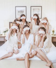 a group of women sitting on top of a bed with blindfolds covering their eyes