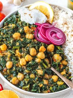 a white bowl filled with rice, spinach and chickpeas next to sliced oranges