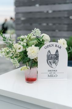 a small vase with white flowers in it and a sign that says open bar drinks miko