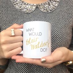 a woman holding a white coffee mug with gold lettering