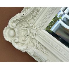 an ornate white framed mirror hanging on the wall