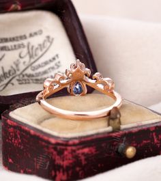 an antique ring with a blue stone sits in a box on a white cloth covered surface