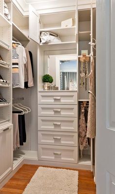 a white closet with lots of drawers and clothes hanging on the shelves, along with a rug