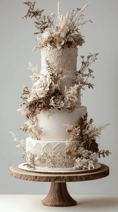 a three tiered white wedding cake with flowers on the top and bottom, sitting on a wooden stand