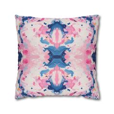 a pink and blue pillow with an abstract design on the front, sitting on a white surface