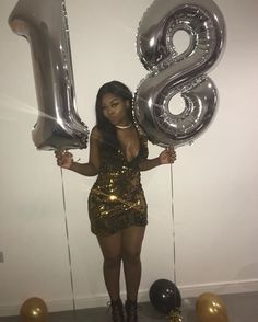 a woman in a gold dress holding two silver balloons and the number eight is 8