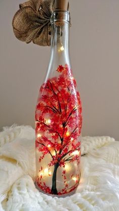 a bottle with lights in it and a tree painted on the inside is sitting on a white blanket