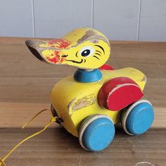 a wooden toy car with a painted face on it's head and wheels, sitting on a wood surface