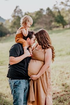 a man and woman holding a baby girl in their arms while standing on the grass