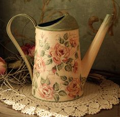 an old watering can with roses painted on it sitting on a doily next to flowers