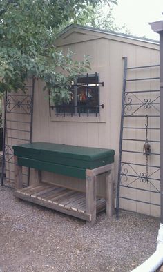 a wooden bench sitting in front of a building next to a tree and fenced yard