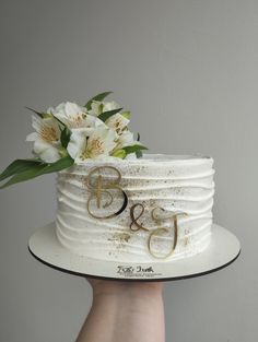 a white cake with gold lettering and flowers on top is being held by a hand