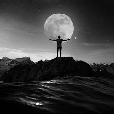 a man standing on top of a rock with his arms outstretched in front of the moon