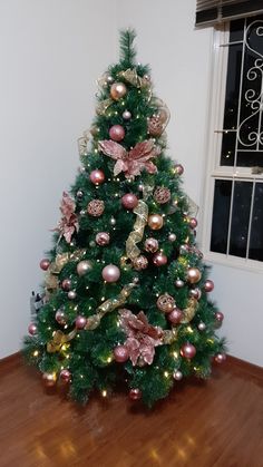 a small christmas tree with pink and gold ornaments on it's branches in front of a window