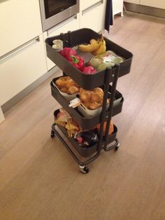 a three tiered cart filled with food on top of a hard wood floor next to an oven