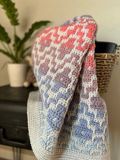 a knitted blanket sitting on top of a table next to a potted plant