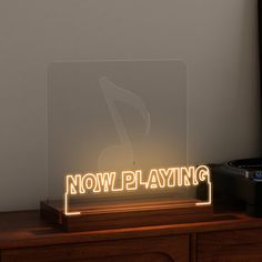 an illuminated sign that says now playing on the side of a wooden table next to a record player