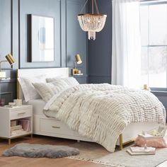 a bedroom with blue walls, white bedding and a chandelier hanging from the ceiling