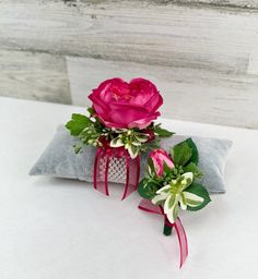 two pink roses sitting on top of a pillow with green leaves and flowers attached to it