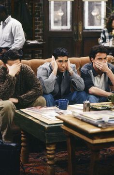 four people sitting on a couch in a living room with one person covering his face