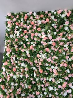 a wall covered in pink and white flowers next to a green plant filled with greenery