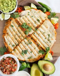 two quesadillas on a cutting board with avocado and salsa in bowls