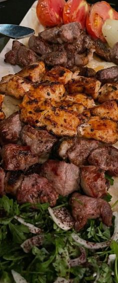 a plate with steak, tomatoes and other food items on it next to a knife