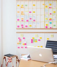 an office desk with a laptop computer on it and sticky notes attached to the wall