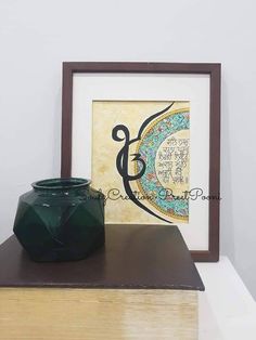 a green vase sitting on top of a wooden table next to a framed art piece