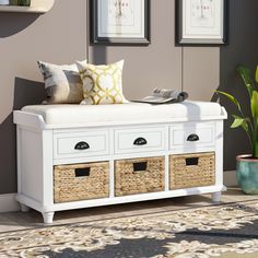 a white bench with baskets underneath it and pictures on the wall behind it in a living room