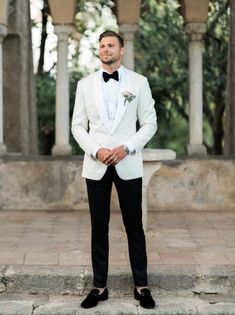 a man in a white tuxedo and bow tie is standing on some steps