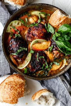 a pan filled with meat and vegetables next to bread on top of a white table