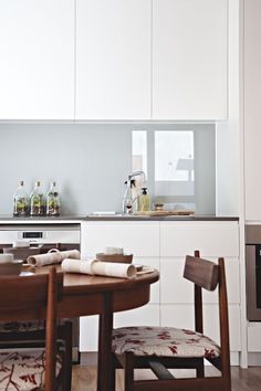 a kitchen with white cabinets and wooden table in the foreground, an oven on the far wall