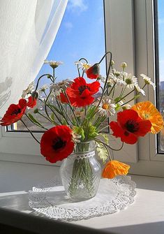 a vase filled with red and yellow flowers on top of a table next to a window