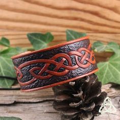 a brown leather ring with an intricate design on the inside, sitting next to a pine cone