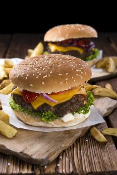 two hamburgers with cheese, lettuce and ketchup on a cutting board