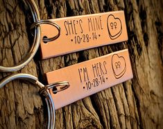 two metal key chains attached to a tree trunk with names engraved on the handles and sides