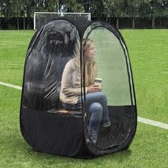 a woman sitting inside of a black tent on top of a green field