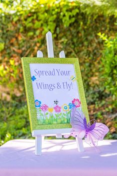 a purple butterfly sitting on top of a table next to a sign that says spread your wings and fly