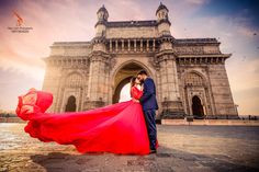 a man and woman standing in front of a large building with a red dress on