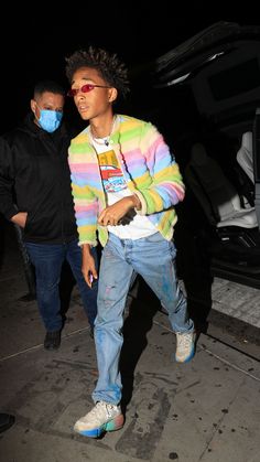 a young man wearing a face mask while walking down the street with another person behind him