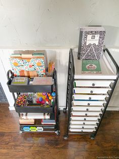 two black metal storage racks with books and toys on top of each other in front of a white wall