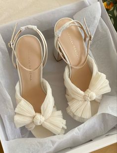 a pair of white high heeled shoes with a bow